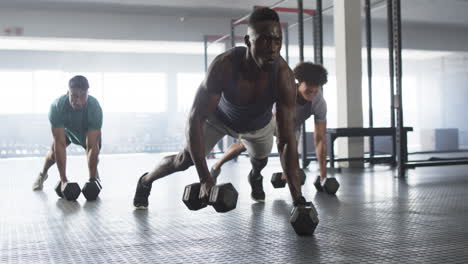 diverse young men training with dumbbells in gym, doing push-up exercises