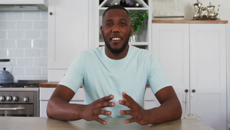 african american man looking to camera talking on video call in kitchen