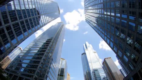 a majestic view of skyscrapers reaching towards the sky with clouds in a blue horizon, capturing the urban landscape from a unique low angle perspective