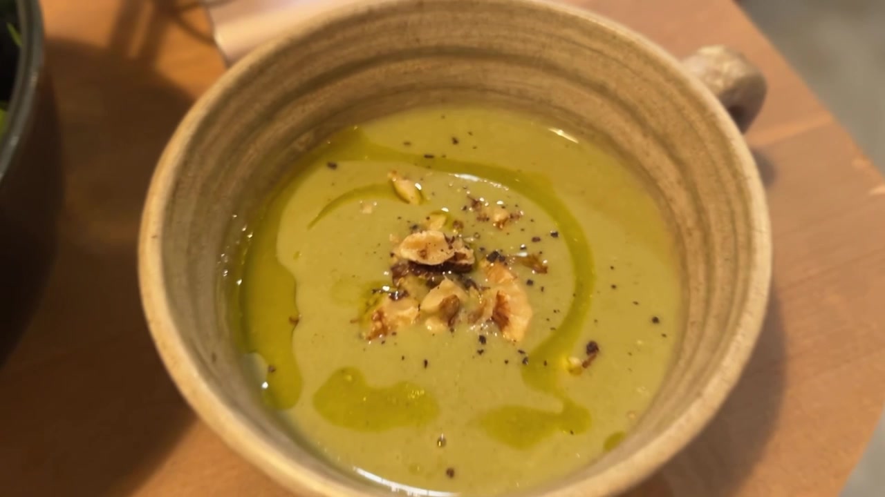 Cremet grøn ærtepurésuppe pyntet med nødder.