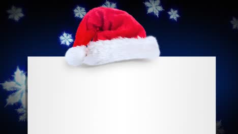 Weihnachtsmütze-über-Einem-Leeren-Plakat-Gegen-Schneeflocken,-Die-Auf-Blauem-Hintergrund-Schweben