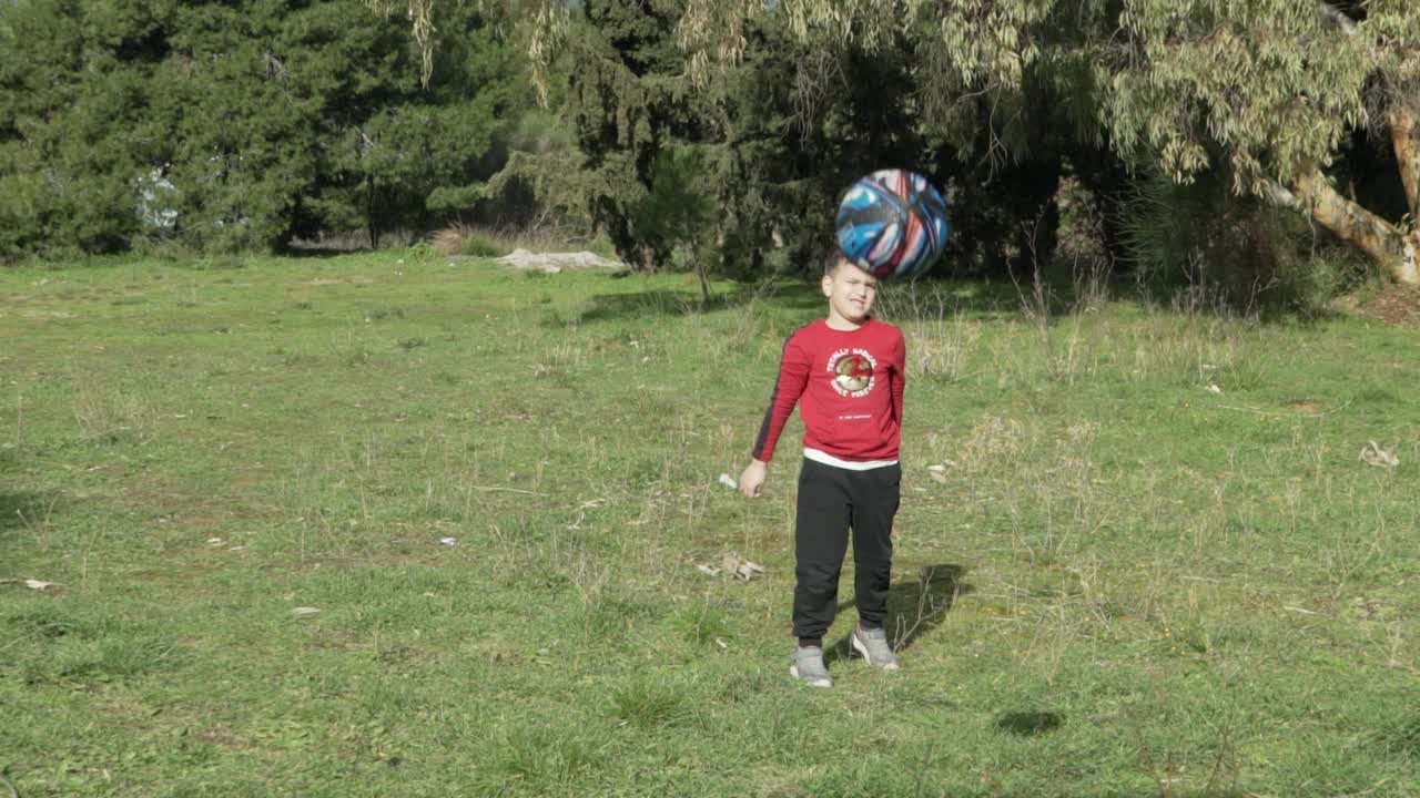 toma en cámara lenta de un niño caucásico pasando una pelota de baloncesto de tamaño pequeño hacia la cámara, haciendo ejercicio en los campos