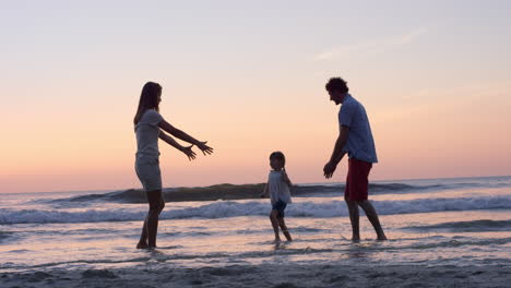 Mutter-Schwingt-Kleines-Mädchen-Um-Glückliche-Familie-Am-Strand-Und-Hält-Händchen-Bei-Sonnenuntergang-Im-Urlaub
