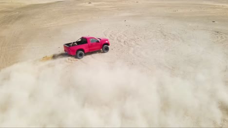 slow motion shot of a red truck sliding and spinning its tires off road in a sandy desert