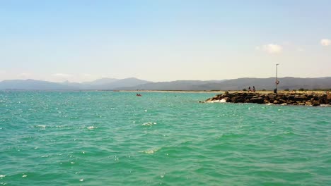 Low-drone-shot-of-turquoise-water-in-the-Mediterranean-coast-of-Castellon-with-mountains-on-the-horizon