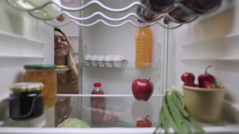 woman looking inside a refrigerator at a donut