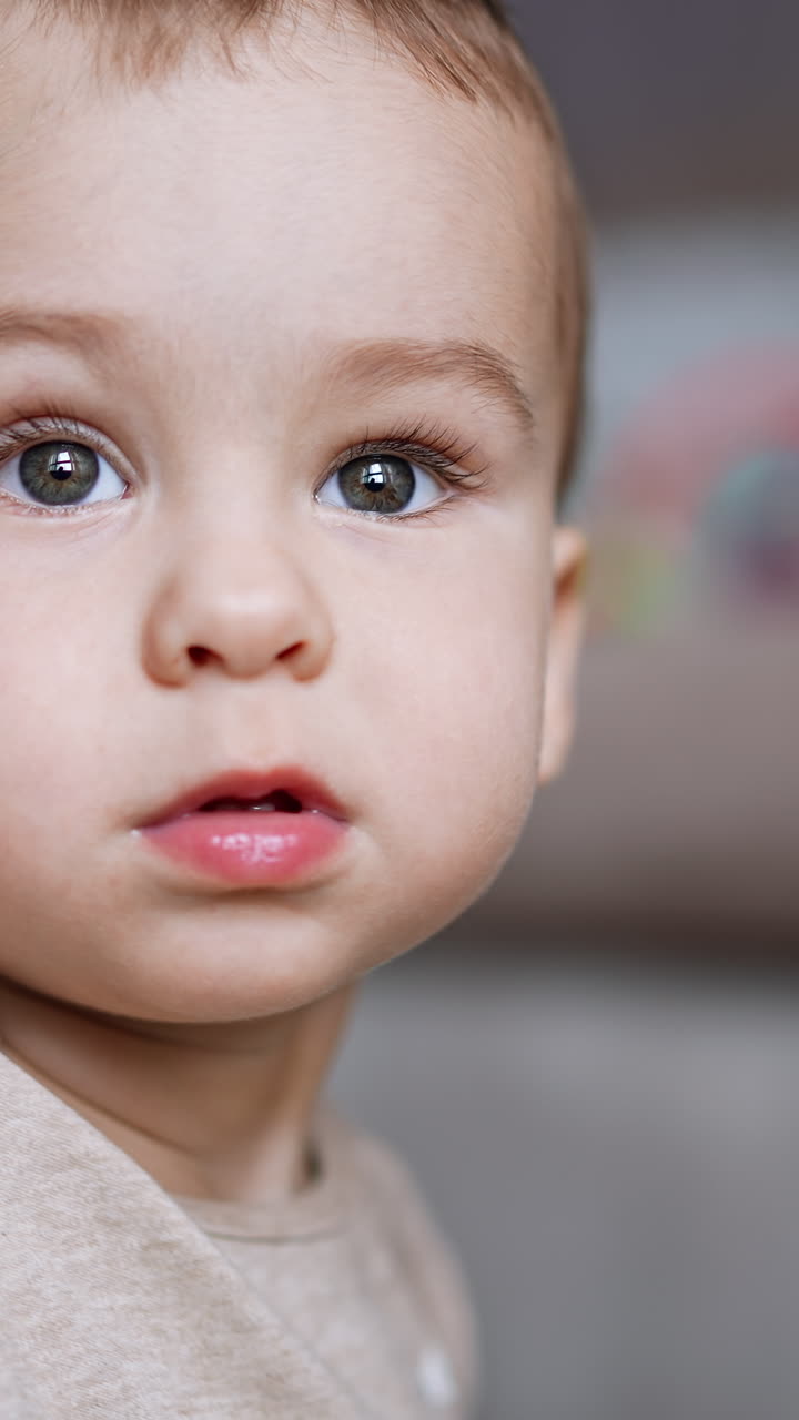 Beautiful Caucasian baby boy looking at camera and up. Close up portrait. Blurred backdrop. Vertical video