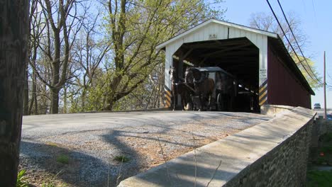 an amish horse and buggy cart pass through a covered bridge in rural lancaster pennsylvania 1