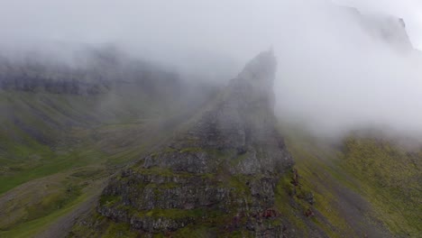 Lebendige-Bilder-Von-Wolken-Sammeln-Sich-An-Einem-Diesigen-Morgen-In-Island-Um-Die-Spitze-Grüner-Felsiger-Berge