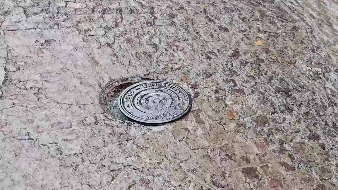Water pressure lifting a manhole cover on a cobblestone street
