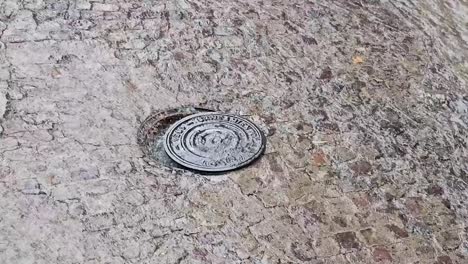 water pressure lifting a manhole cover on a cobblestone street