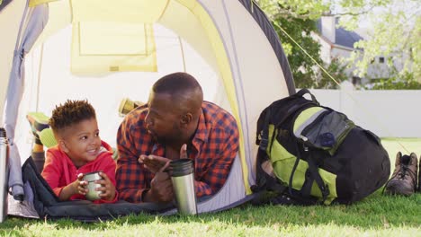 Happy-african-american-father-and-his-son-laying-in-tent-in-garden