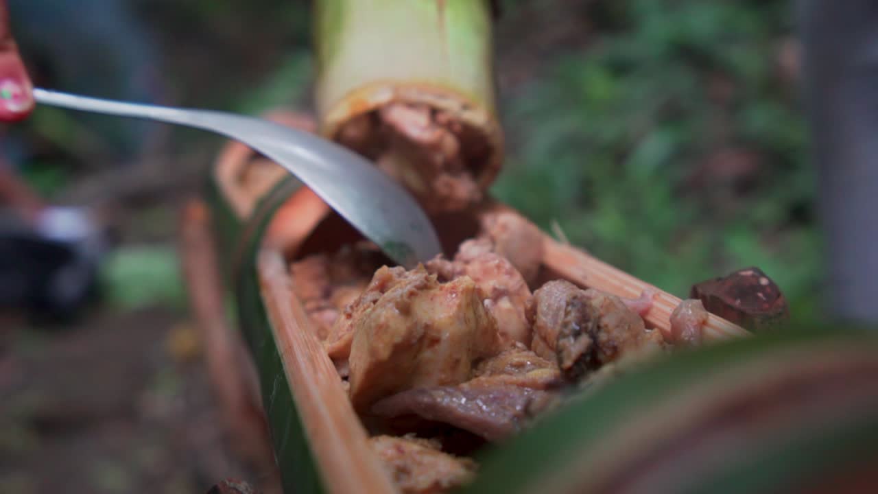 Campers throw in steamed meat into bamboo shoot as a bowl to eat