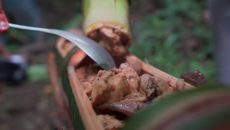 campers throw in steamed meat into bamboo shoot as a bowl to eat