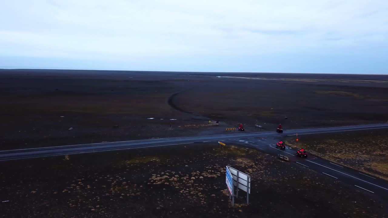 Aerial view of bright red quad bikes going off road through Iceland black sand beach