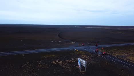 aerial view of bright red quad bikes going off road through iceland black sand beach