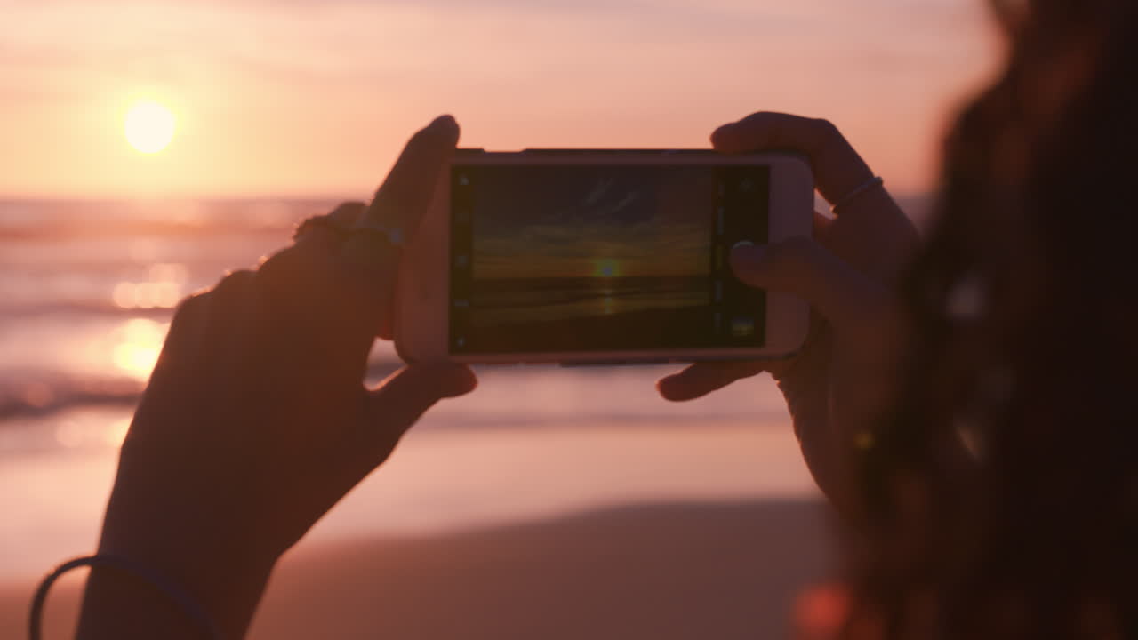 mujer joven en la playa usando un teléfono inteligente tomando una foto de una hermosa puesta de sol disfrutando de compartir la experiencia de viaje de las vacaciones de verano en las redes sociales