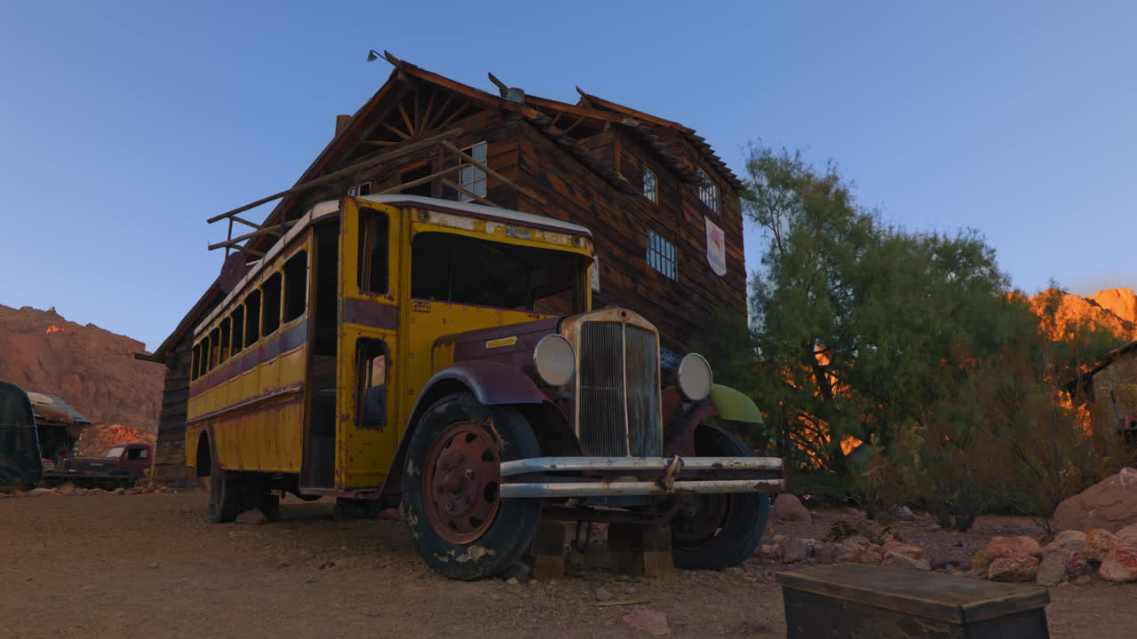 Old broken down school bus sits abandoned in front of an old decrepit building.