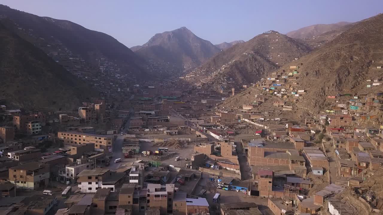 A sprawling cityscape merges with hillside settlements in a dramatic aerial view. Earth-toned buildings contrast with rugged mountains. Ideal for documentary, editorial, and urbanization studies.