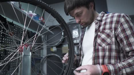technician adjusts bicycle spokes and repairs wheel in bike store workshop. mechanic adjusts bike spokes and repair wheel. a velomechanic at work, checks tension of the spoke with a special tool.