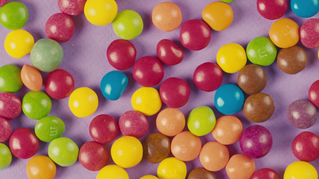 Colorful dragee candies on purple background. Summer bright texture studio shot for store, supermarket, close-up top view. Children sweets made of sugar, mix of lollipops. Beautiful bonbons.