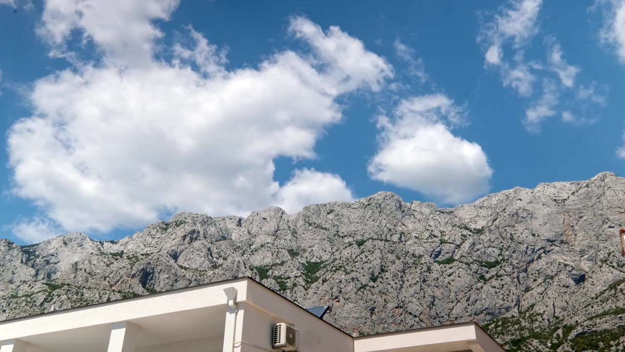 Kroatiske kystbjerge. Denne time-lapse fanger skyerne, der suser og forvandler sig, mens de bevæger sig hurtigt over bjergtoppene. Toppen af et sommerhus ses i forgrunden