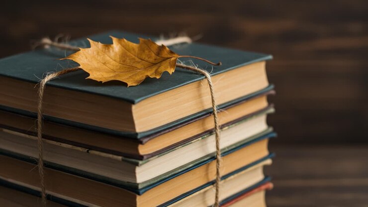 A stack of books tied together with twine, featuring an autumn leaf on top, representing the beauty of reading and the changing seasons in a cozy setting