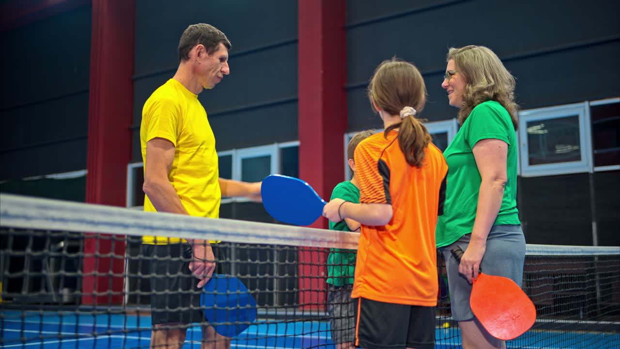 To voksne og to barn som slår hverandre high-five etter å ha spilt pickleball på en blå innendørsbane