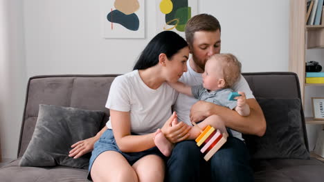 happy parents with their little son sitting on sofa in living room and looking at camera during a video call at home