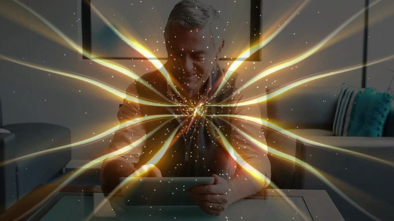 Senior man tapping tablet activating golden ribbons above table while watching pattern in tech demo