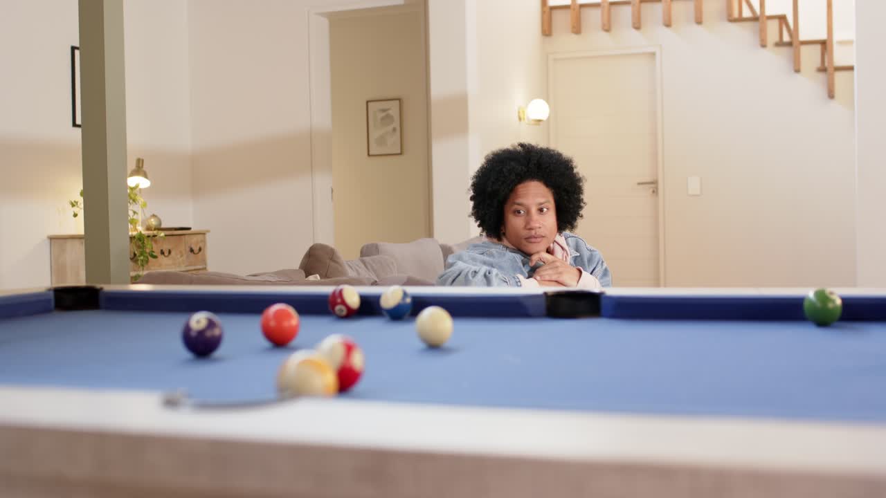 Noticing billiard balls on blue pool table, mid-adult man leaning on hands at home calculating shot