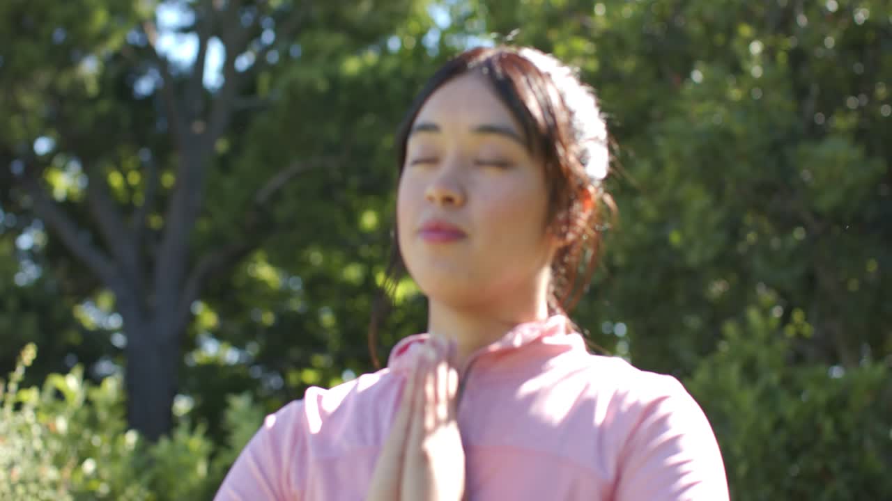 胸の前で手のひらを合わせている多様な友人たち。カメラがパンすると女性が現れ、二人とも公園で安らぎを求めている。
