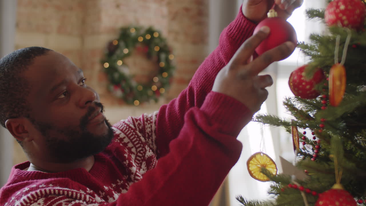 hombre negro alegre decorando el árbol de navidad en casa