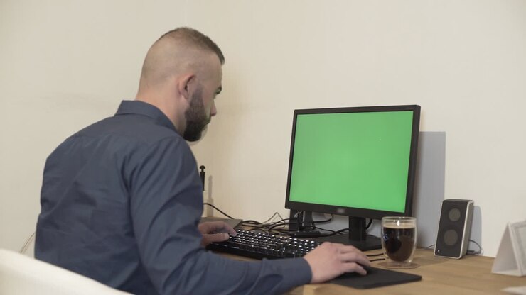 Junger Mann tippt auf Tastatur mit Greenscreen auf dem Monitor.