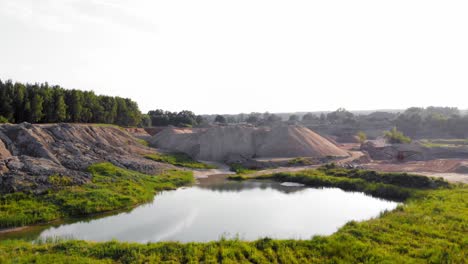 Drone-dolly-shot-of-dunes,-pits-and-a-pond-in-a-quarry-,-showing-contrast-between-nature-and-industry