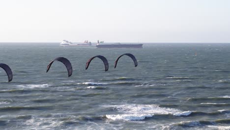 cuatro cometas de viento oscuro alineadas juntas deslizándose en el aire frente a barcos de carga