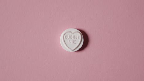 mano recogiendo caramelos de corazón con un mensaje de abrazos sobre fondo rosa