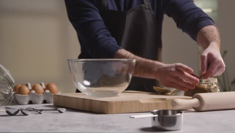 close up of man in kitchen at home adding ingredients to bowl to bake cake