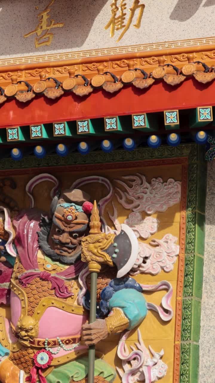 Pystysuuntainen lähikuva värikkäästä soturipatsaasta ja koristeellisista perinteisistä kattotiilistä Hongkongissa