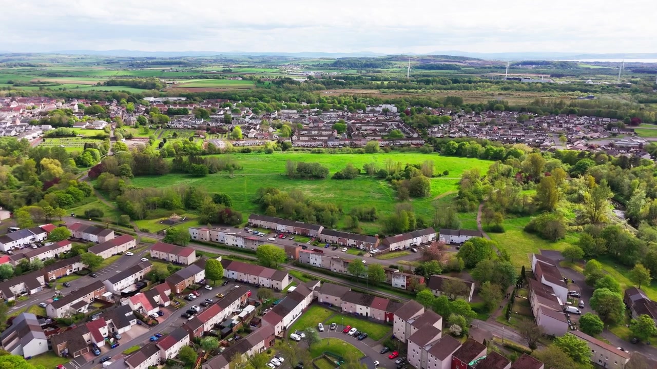 Aerial dolly forward drone footage over Dreghorn, Ayrshire, Scotland showing residential housing, green countryside, open fields and suburban landscape
