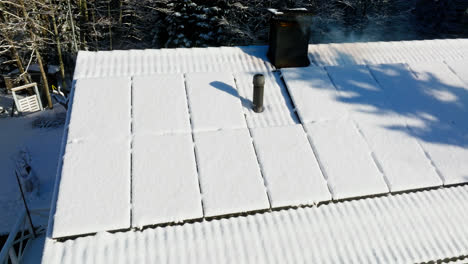 drone dando vueltas iluminado por el sol, cubiertas de nieve células solares en una casa con una chimenea humeante