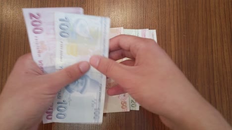 A-teenager-sorting-each-banknote-of-Turkish-lira-by-value,-with-portraits-of-famous-Turkish-figures-from-science,-literature,-and-music-on-top