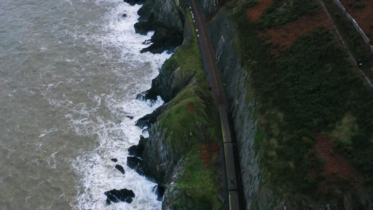Vista aerea dall'alto del DART (Irish Rail) che supera un ponte faunistico lungo la costa di Bray Head durante la sera