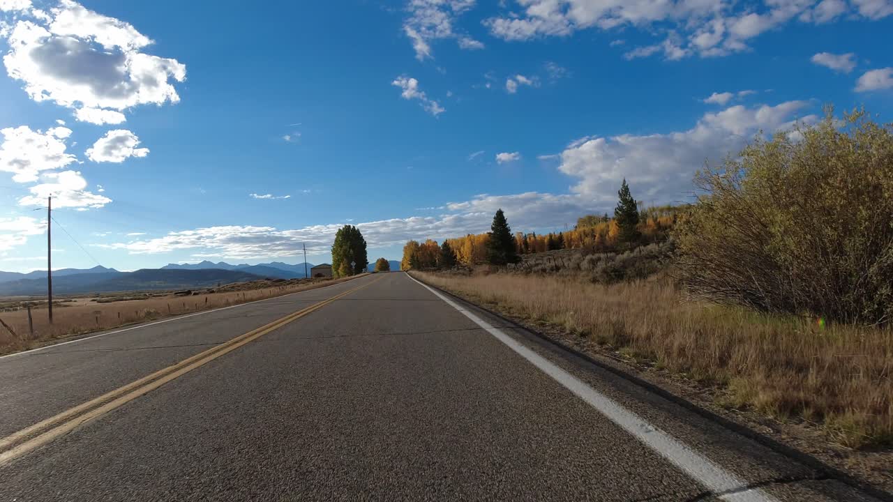 Toma de conducción - Carretera 14 en Colorado durante un hermoso otoño, con álamos dorados a un lado y tierras de cultivo rurales al otro.