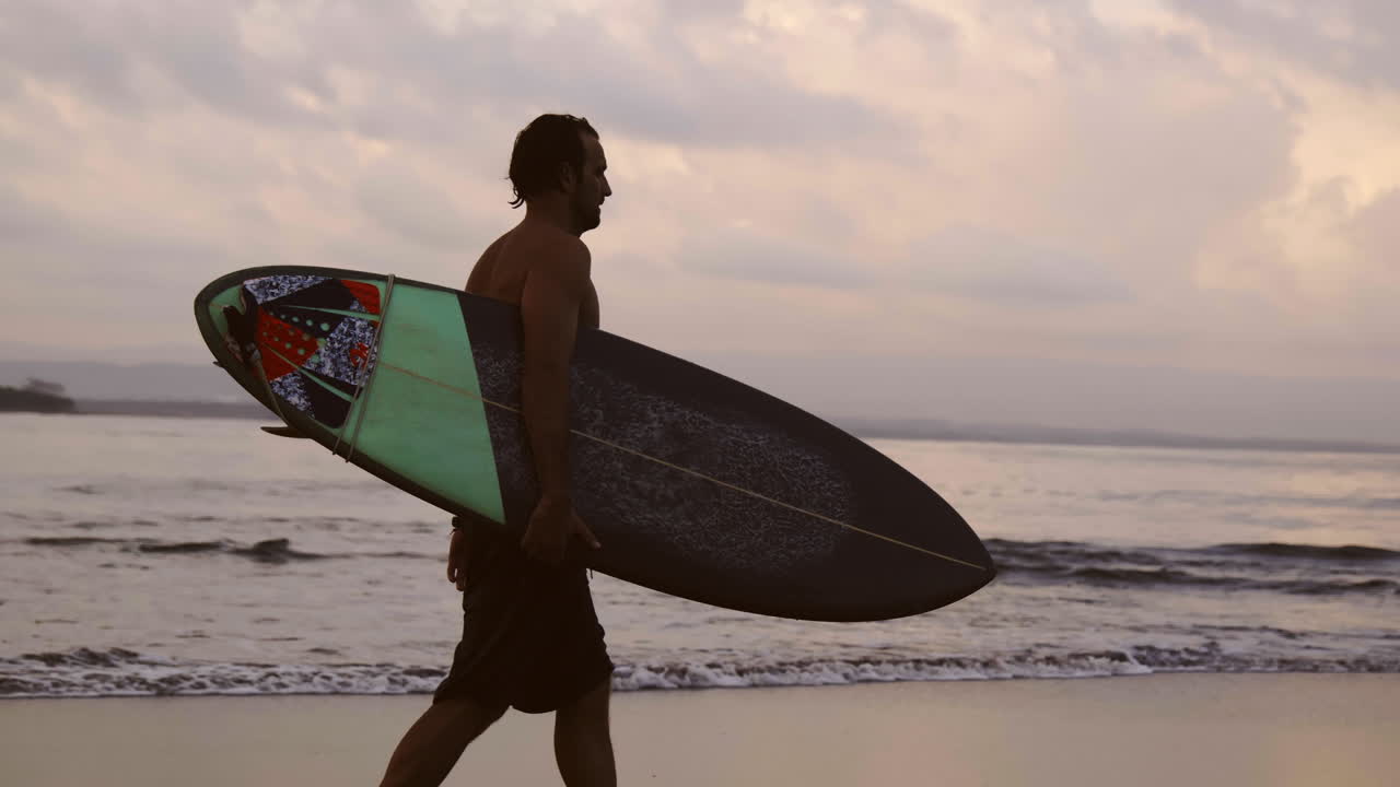 Surfer carrying surfboard at sunset on beach