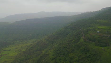 a drone captures lush green mountains of panchgani, maharashtra, draped in monsoon mist. rolling hills vanish into the fog, creating a serene and mystical landscape 4k