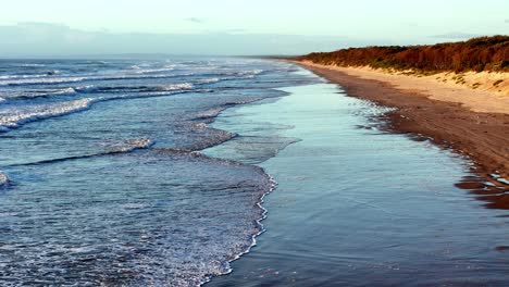 Suaves-Olas-Rompiendo-En-La-Orilla-Arenosa-De-Una-Playa-Aislada,-Una-Costa-Serena-Que-Se-Extiende-En-La-Distancia