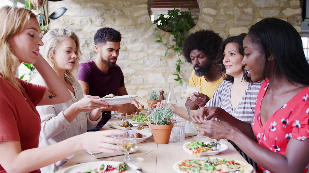 A multi-ethnic group of mixed age adult friends eating lunch together at table in a restaurant raise their glasses in a toast, side view