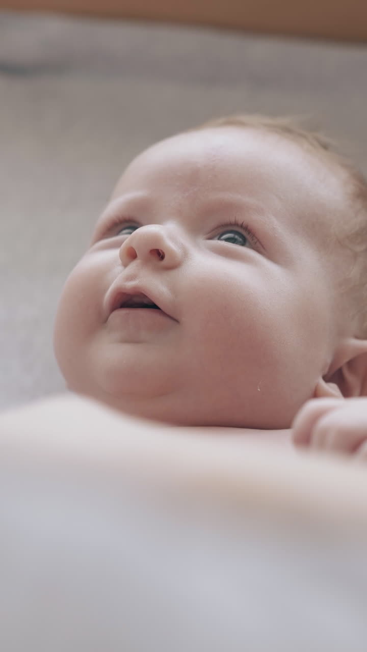 concentrated newborn boy with short fair hair lies on changing table and nurse cross baby arms making massage closeup