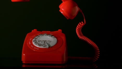 red phone receiver falling on dial phone on black background